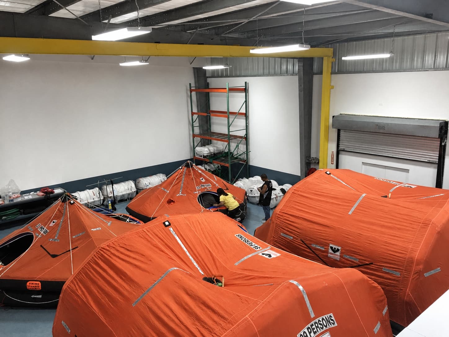 Technicians working among open liferafts inside The Safety Pelican workshop