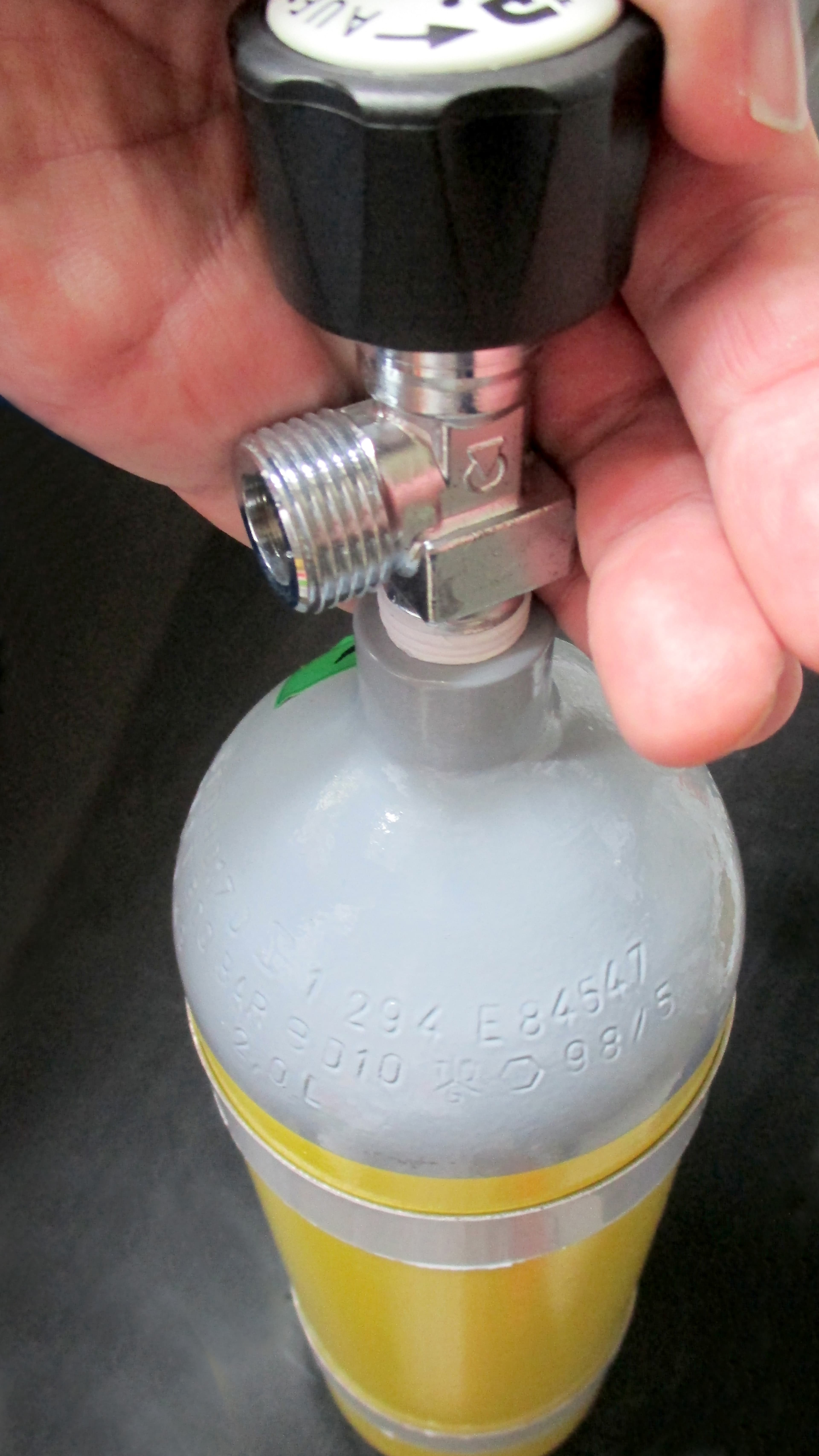 Rows of stamped letters, numbers and symbols around the metal shoulder of a diving cylinder